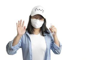 asiatische junge frau in einem lässigen blauen t-shirt und einer weißen kappe sprüht und wäscht ihre hand mit einer kleinen alkoholsprühflasche auf ihrer hand. weißes, klares Hintergrundstudiolicht. foto