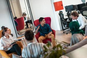 Multiethnisches Startup-Business-Team mit Brainstorming im Entspannungsbereich der modernen Büroeinrichtung, das an Laptop und Tablet-Computer arbeitet foto
