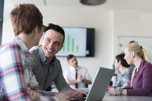 Junge Geschäftspaare, die am Laptop arbeiten, Geschäftsleute gruppieren sich auf Treffen im Hintergrund foto