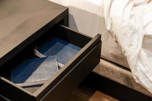 Bett mit weißem Laken und neben einem hölzernen Schubladenständer und einem Notizbuch im Inneren. foto