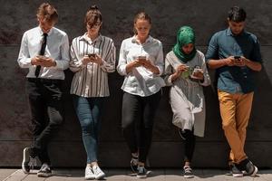 multiethnische gruppe von lässigen geschäftsleuten, die während der kaffeepause von der arbeit vor der schwarzen wand draußen telefonieren foto