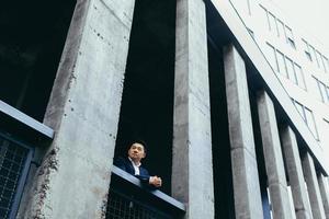 junger asiatischer geschäftsmann, der in der nähe eines modernen schwarzen bürogebäudes aus beton steht foto