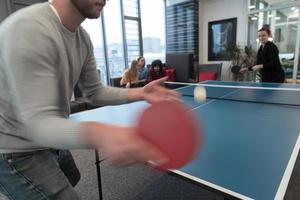Junger Start-up-Geschäftsmann und -frau, die Tischtennis in modernen kreativen Büroräumen spielen, treffen sich und Brainstorming im Hintergrund foto