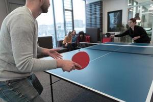 Junger Start-up-Geschäftsmann und -frau, die Tischtennis in modernen kreativen Büroräumen spielen, treffen sich und Brainstorming im Hintergrund foto
