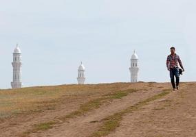 Mann mit Sonnenbrille und Umhängetasche zu Fuß von einer Moschee in Nur-Sultan, Kasachstan foto