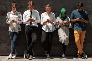 multiethnische gruppe von lässigen geschäftsleuten, die während der kaffeepause von der arbeit vor der schwarzen wand draußen telefonieren foto