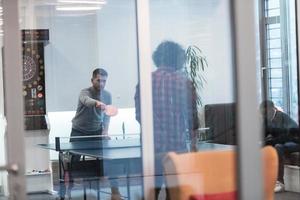 Zwei junge Start-up-Geschäftsleute, die in modernen kreativen Büroräumen Tischtennis spielen, haben Treffen und Brainstorming im Hintergrund foto