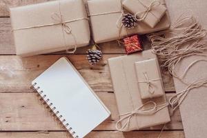 Weihnachtsgeschenkbox Verwenden Sie braunes Recyclingpapier und ein Notizbuch und Tannenzapfen auf einem Holztisch. foto