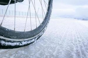 Nahaufnahme des Fahrradrades auf weißer, vereister Straße. Radfahren unter extremen Winterbedingungen Konzept und Winterreifen foto