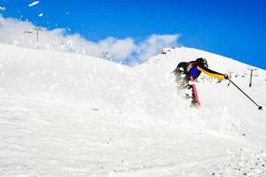 dynamisches bild eines skifahrers auf der piste in den alpen. Skifahrerin im weichen Schnee. aktiver winterurlaub, skifahren an sonnigen tagen. skifahrten auf der strecke mit wirbeln von frischem schnee foto