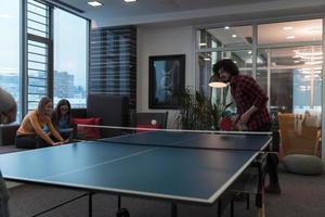 Zwei junge Start-up-Geschäftsleute, die in modernen kreativen Büroräumen Tischtennis spielen, haben Treffen und Brainstorming im Hintergrund foto