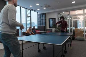 Zwei junge Start-up-Geschäftsleute, die in modernen kreativen Büroräumen Tischtennis spielen, haben Treffen und Brainstorming im Hintergrund foto