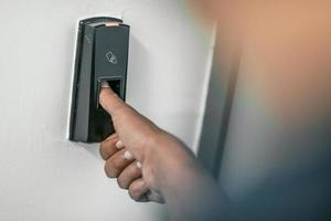 Mann drückt Fingerabdruckscanner auf Alarmanlage im InnenbereichFingerabdruckscan zum Entriegeln des Türsicherheitssystems foto