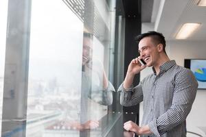 Junger Geschäftsmann, der im Büro am Smartphone spricht foto