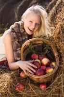 schöne blonde lächelnde Frau mit Äpfeln im Korb am Bauernhof foto