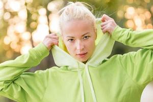 selbstbewusste sportliche Frau, die modischen grünen Kapuzenpulli trägt.
