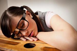 gelangweilte, nerdige junge Studentin, die auf der Schulbank schläft