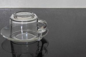 Leere umgedrehte transparente Kaffeetasse auf einem durchsichtigen Teller mit einem Löffel auf dem Tisch. foto