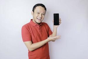 Ein Porträt eines glücklichen asiatischen Mannes lächelt und zeigt Kopierraum auf seinem Smartphone mit rotem Hemd, das durch einen weißen Hintergrund isoliert ist foto