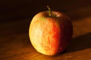 Apfel auf dem Tisch, der von der Nachmittagssonne beleuchtet wird foto