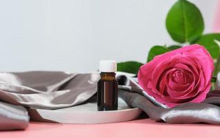 Rosenblütenöl. Ätherisches Öl zur Gesichtspflege und Hautbefeuchtung. eine Flasche Aromaöl und frische rosa Rose auf Seidenblatt. foto