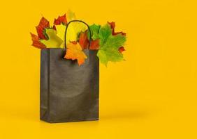 Herbstlaub in einer Tasche auf orangefarbenem Hintergrund. saisonale komposition für layouts, vorlage mit platz für text. Konzept - Herbstverkauf, Einkaufsbummel foto