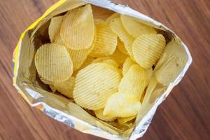 Kartoffelchips in offener Snacktüte hautnah auf dem Tischboden foto