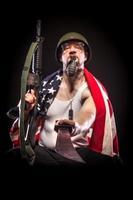 Soldat trägt amerikanische Flagge, hält Granate im Mund, Machete foto