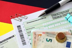deutsches einkommensteuererklärungsformular mit stift und europäischen euro-geldscheinen liegt auf der flagge in der nähe. steuerzahler in deutschland verwenden euro-währung, um steuern zu zahlen foto