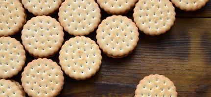 Ein runder Sandwichkeks mit Kokosfüllung liegt in großen Mengen auf einer braunen Holzoberfläche. Foto von essbaren Leckereien auf einem hölzernen Hintergrund mit Kopierraum