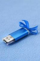 Eine leuchtend blaue USB-Flash-Speicherkarte mit einer blauen Schleife liegt auf einer Decke aus weichem und pelzigem hellblauem Fleece-Stoff. klassisches weibliches Geschenkdesign für eine Speicherkarte foto