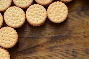 Ein runder Sandwichkeks mit Kokosfüllung liegt in großen Mengen auf einer braunen Holzoberfläche. Foto von essbaren Leckereien auf einem hölzernen Hintergrund mit Kopierraum