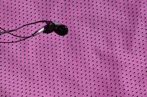schwarze Kopfhörer liegen auf der violetten Sportbekleidung aus Polyester-Nylon-Faser. das konzept des musikhörens während des sporttrainings mit moderner technologie foto