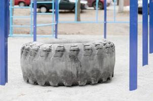 Ein großer schwarzer Reifen gegen einen Straßensportplatz zum Training von Leichtathletik und Crossfit. sportliche Fitnessgeräte im Freien. Makrofoto mit selektivem Fokus und unscharfem Hintergrund foto
