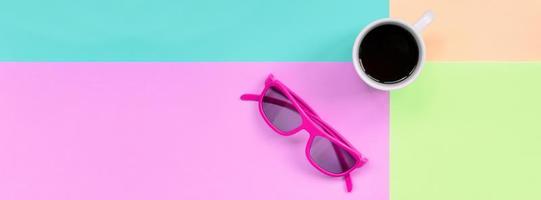 Kleine weiße Kaffeetasse und rosafarbene Sonnenbrille auf dem Hintergrund von Modepastellrosa, Blau, Koralle und Limettenfarben foto