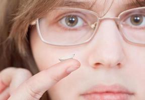Mädchen mit Brille hält Kontaktlinsen foto
