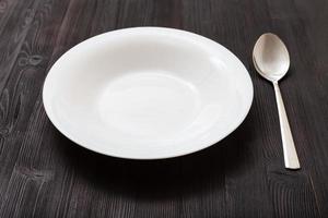 weißer tiefer Teller und Stahllöffel auf braunem Brett foto