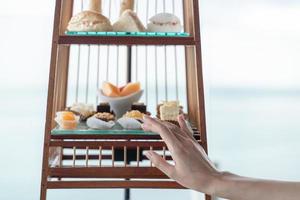 Frau Hand mit einer Reihe von luxuriösen traditionellen Nachmittagstee mit Dessert im Vogelkäfig serviert. foto