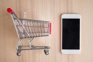 Handy mit Einkaufswagen auf Holztisch Hintergrund Online-Shopping-Konzept foto
