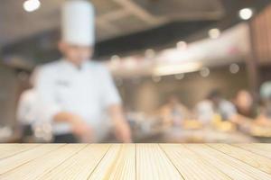 leere Holztischplatte mit Küchenchef, der in der Restaurantküche kocht, unscharfer, defokussierter Hintergrund foto