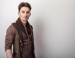 attraktiver junger Mann in einer braunen Pulloverpose im Studio.