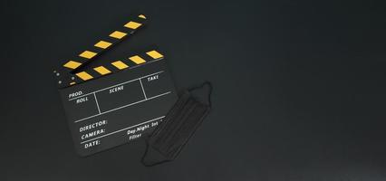 gelbe klappe oder filmtafel mit schwarzer gesichtsmaske oder medizinischer maske isoliert. es wird in der film-, filmproduktions- und kinoindustrie auf schwarzem hintergrund verwendet. covid-19 oder soziales distanzkonzept. foto