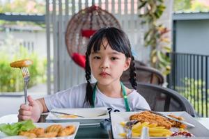 asiatisches junges Mädchen, das Chicken Nuggets Fast Food auf dem Tisch isst. foto