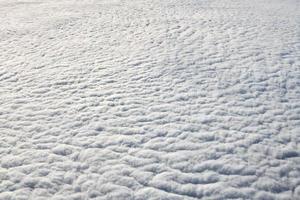 über den wolken draufsicht aus dem flugzeugfenster, dicke weißblaue wolken sehen aus wie weicher schaum foto