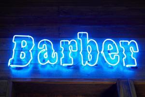 blaue Neonwand mit leuchtender Barber-Inschrift im Loft-Barbershop-Interieur, Lichtstreifen foto