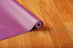 eine fliederfarbene yogamatte liegt in einer rolle auf dem holzboden ausgebreitet. foto