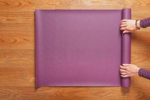Ein Mädchen legt vor einer Trainingspraxis zu Hause auf einem Holzboden eine lila Yogamatte aus. foto