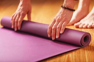 Die Hände einer Frau legen vor einer Trainingspraxis zu Hause auf einem Holzboden eine lilafarbene Yoga- oder Fitnessmatte aus. foto