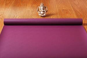 Auf dem Holzboden liegt eine lilafarbene Yogamatte mit einer Ganapati-Figur foto