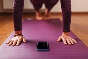 ein mädchen macht yoga mit einem smartphone im asana-stand auf einer lila matte. foto